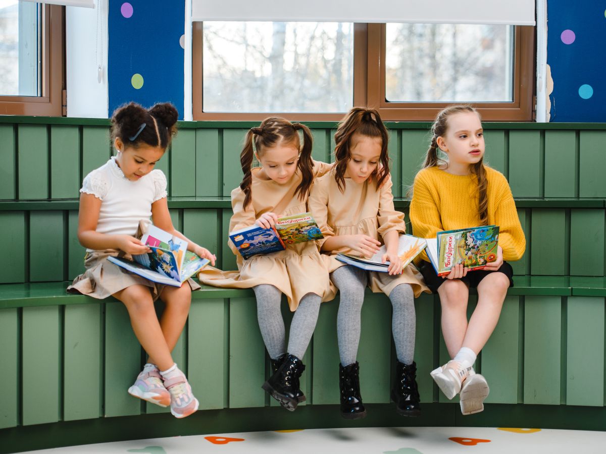 Cuatro niñas leen libros ilustrados sentadas en un banco