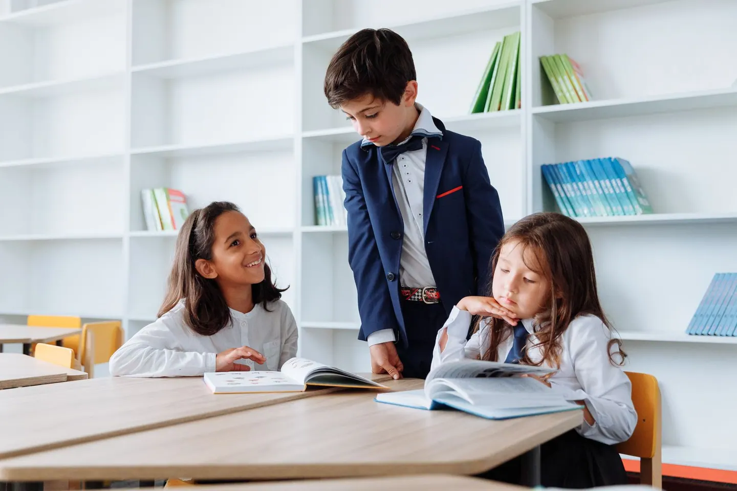 Tres estudiantes comparten libros alrededor de una mesa