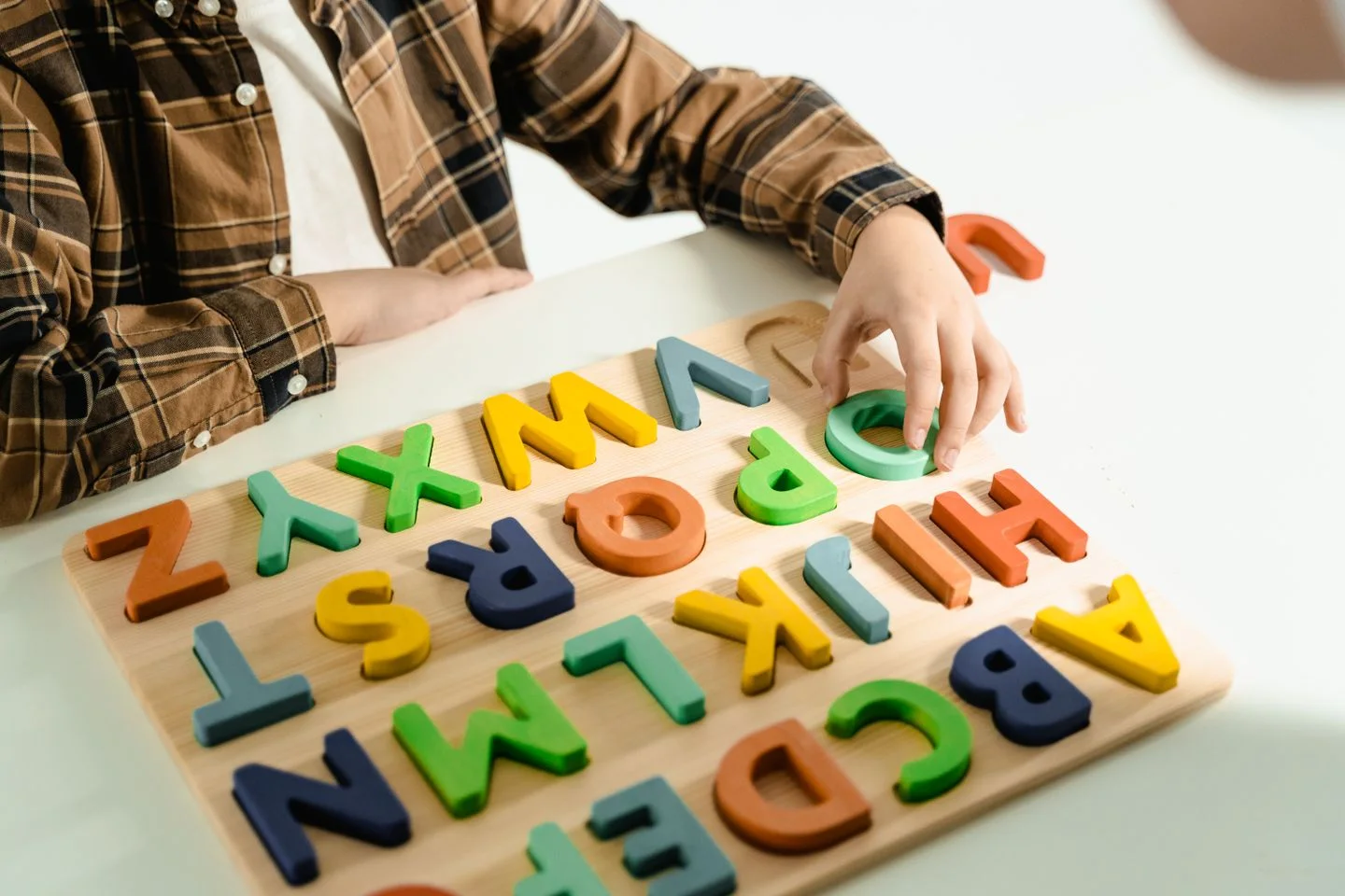 Un niño encaja letras de colores en un tablero de madera