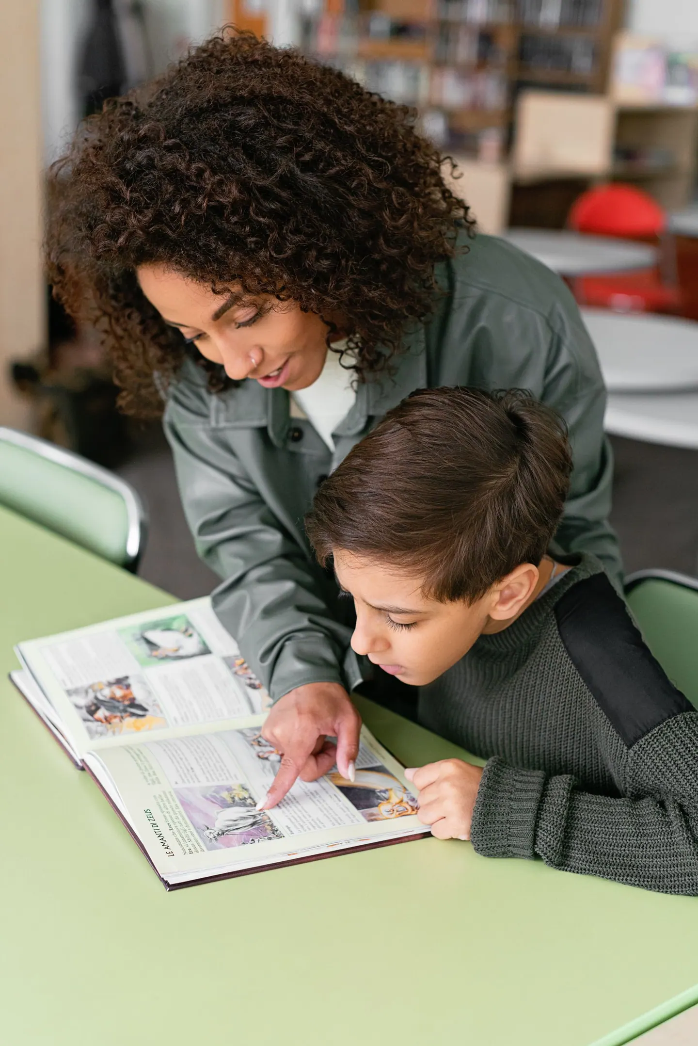 Una adulta acompaña a un niño mientras leen juntos un libro ilustrado