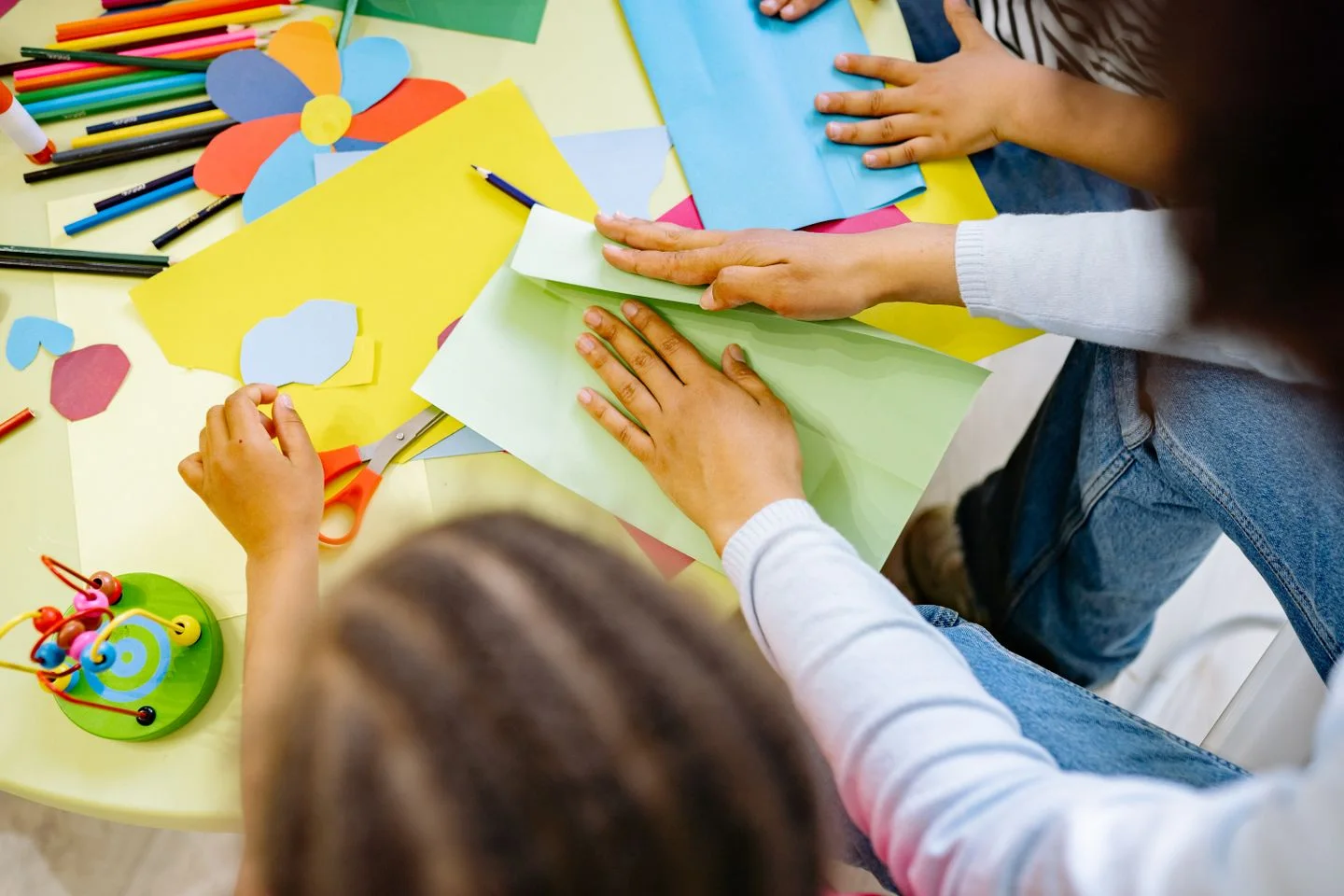 Niños y una adulta crean figuras con papeles de colores alrededor de una mesa